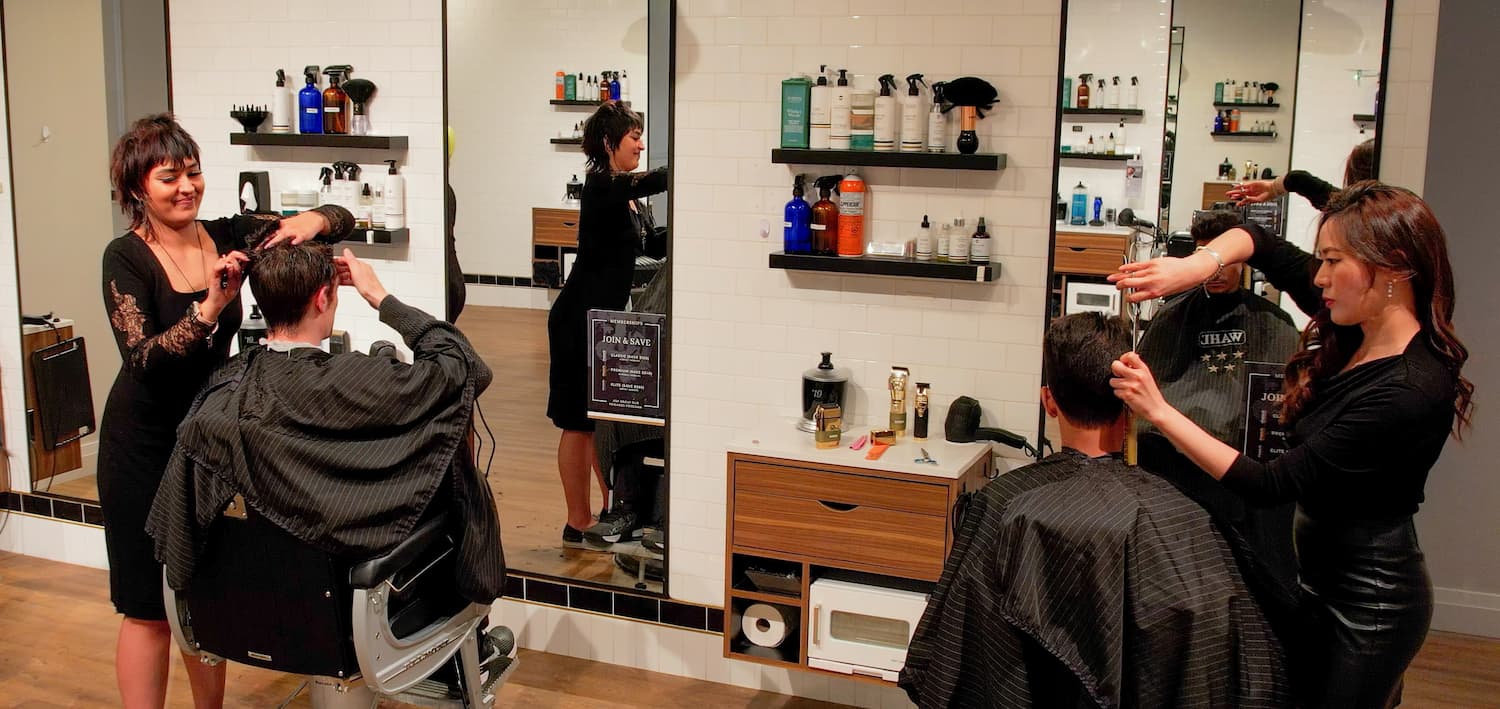 a line of barber chairs with customers and stylists in a modern classy barber shop